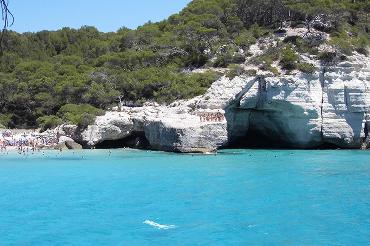Locals diving from a rock into clear turquoise water at Cala Mitjana